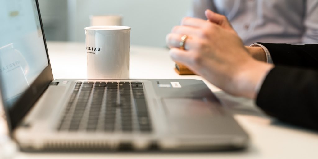 Närbild på en laptop, en mugg och händer